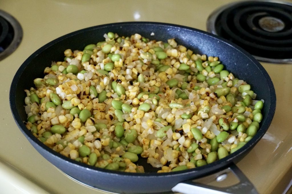 Edamame, corn, onion and garlic sautéeing in a large skillet.