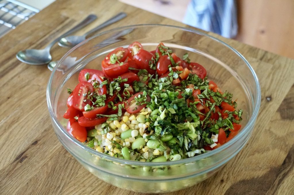 All of the ingredients for the succotash spilled into a large glass salad bowl.