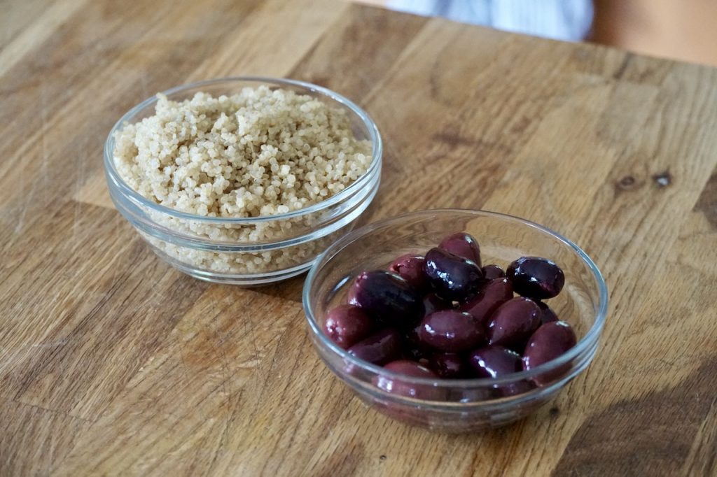 Bowls containing cooked quinoa and halved, pitted black olives.