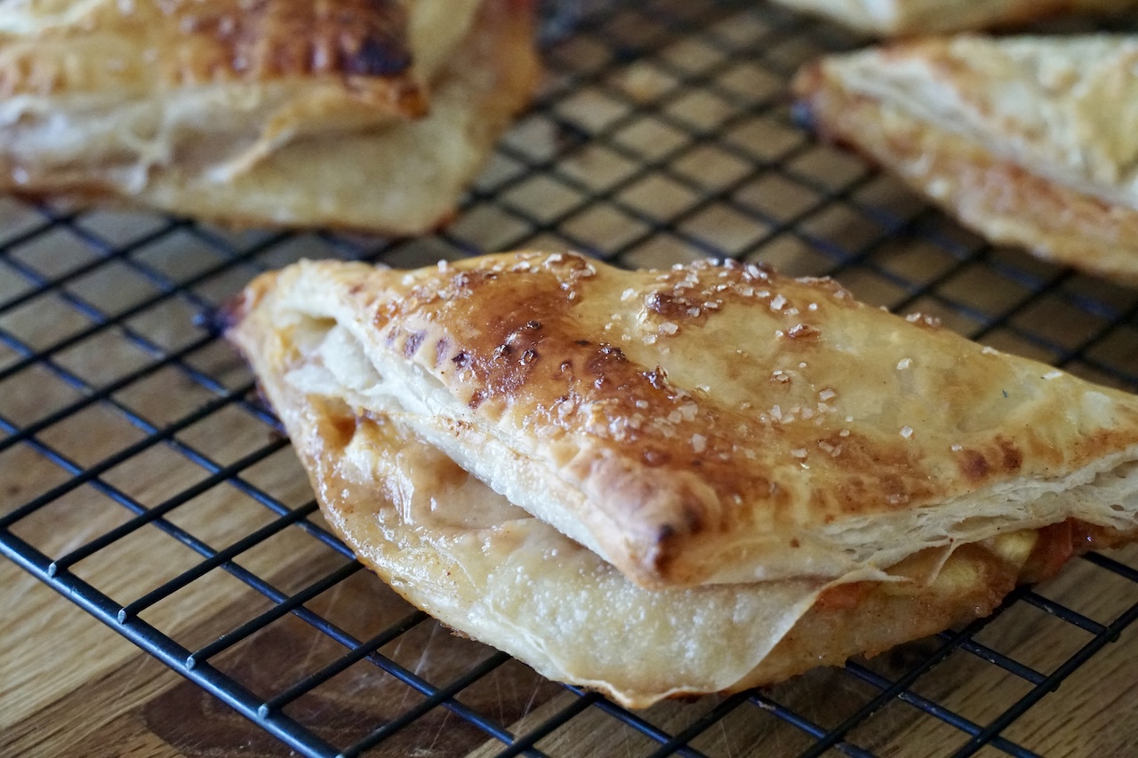 A close up photo of a peach turnover where the filling is oozing out of the folded puff pastry.