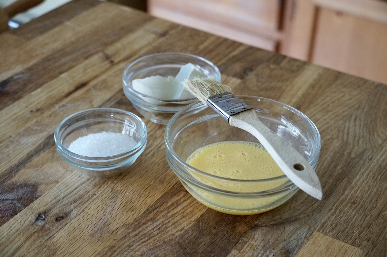 A bowl containing sanding sugar and another containing a whisked egg.