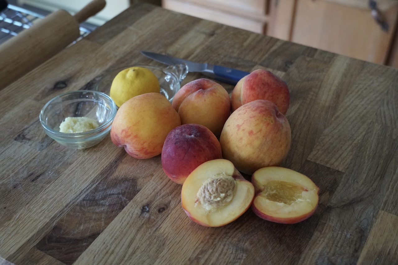 Fresh peaches resting on a cutting board next to a knob of ginger and freshly squeezed lemon juice.