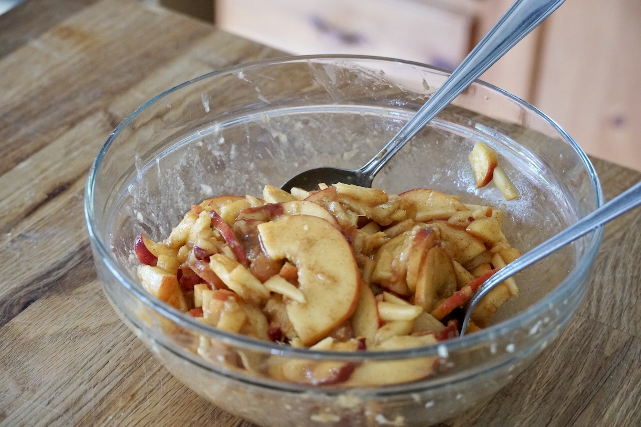 The prepared fresh peaches tossed together in a bowl with the sugar and spice mixture.