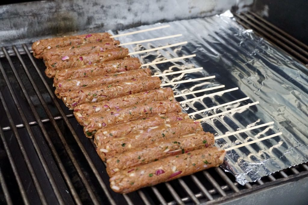 The kofta kebabs laid onto the hot grill with the skewers protected from burning.