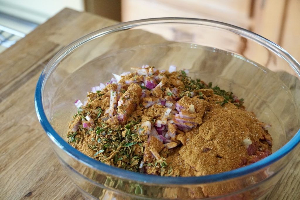 Everything needed to create the meat mixture assembled in a large glass bowl.