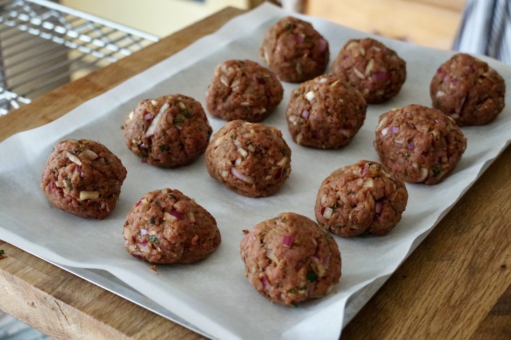 Twelve equal portions of the kofta meat mixture shaped into meat balls.