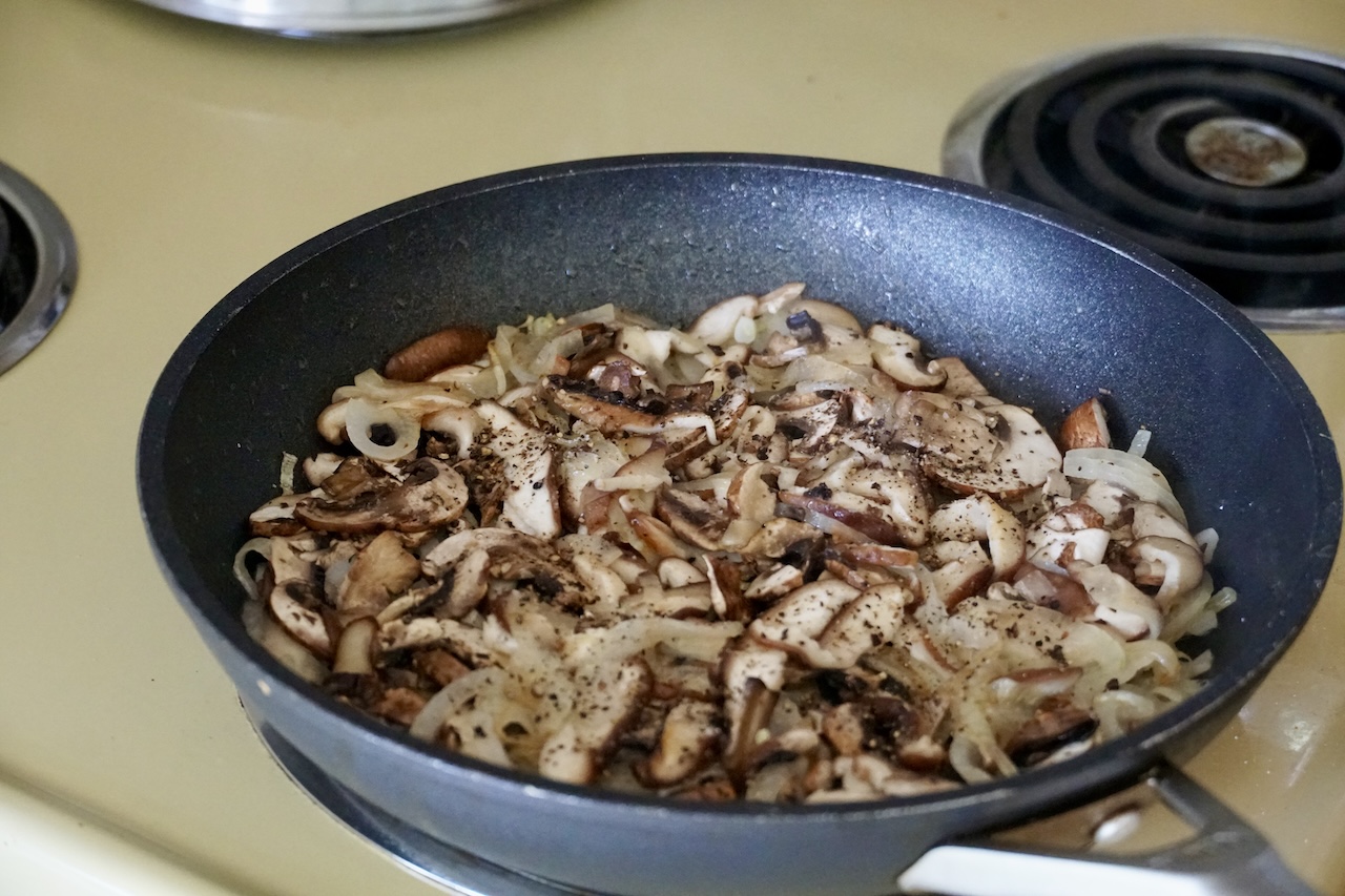 A skillet filled with sautéed mushrooms, onions, chopped chives and balsamic vinegar.