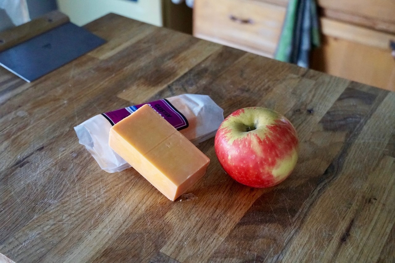 A wedge of sharp Canadian cheddar cheese and a Honeycrisp apple resting on a cutting board.