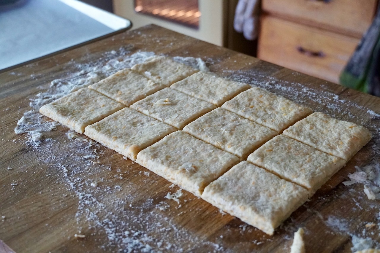 The biscuit dough rolled out in a large rectangular shape cut into 12 square biscuit shapes.