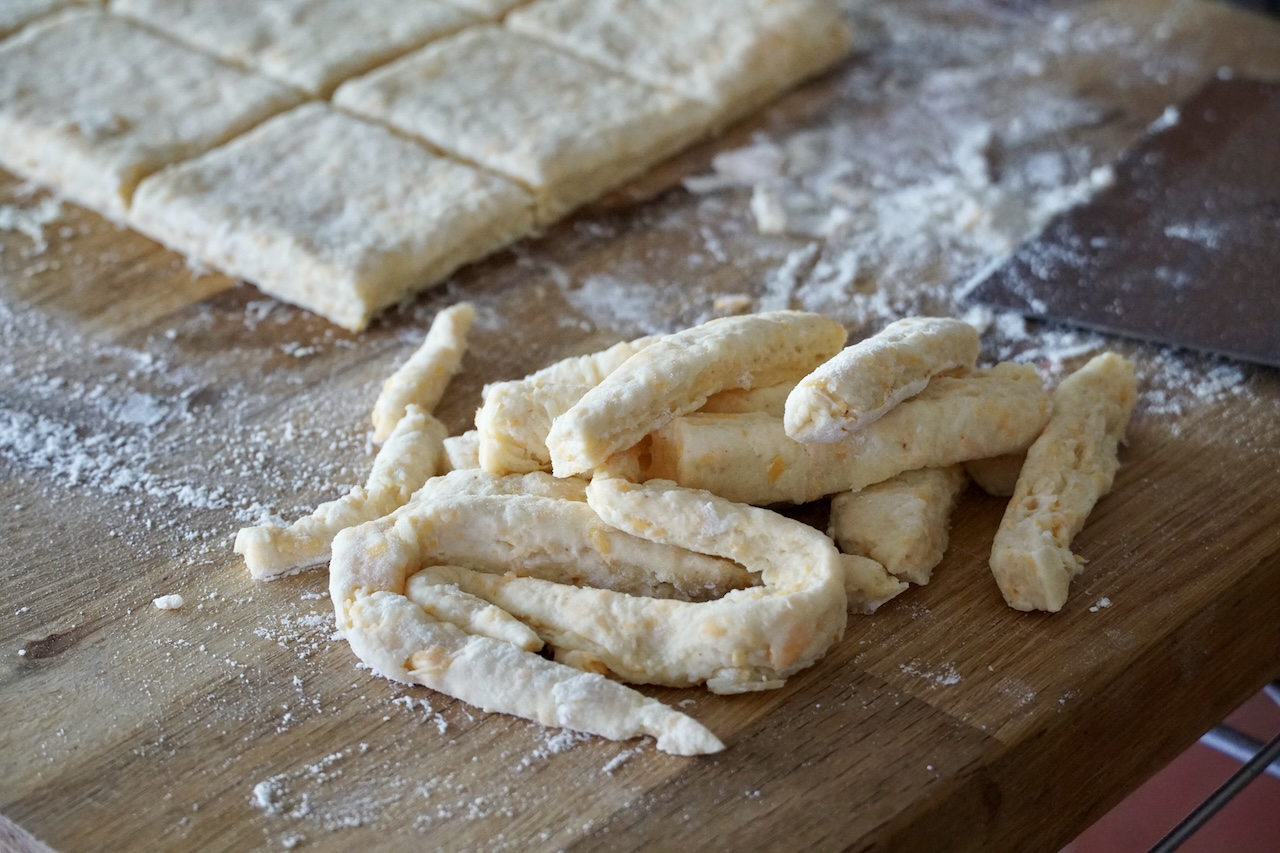 A pile of biscuit dough scraps gathered to the side of the biscuits.