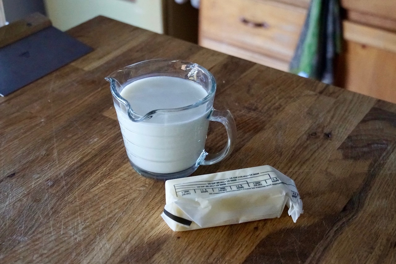 A liquid measure containing whole milk and a stick of unsalted butter.