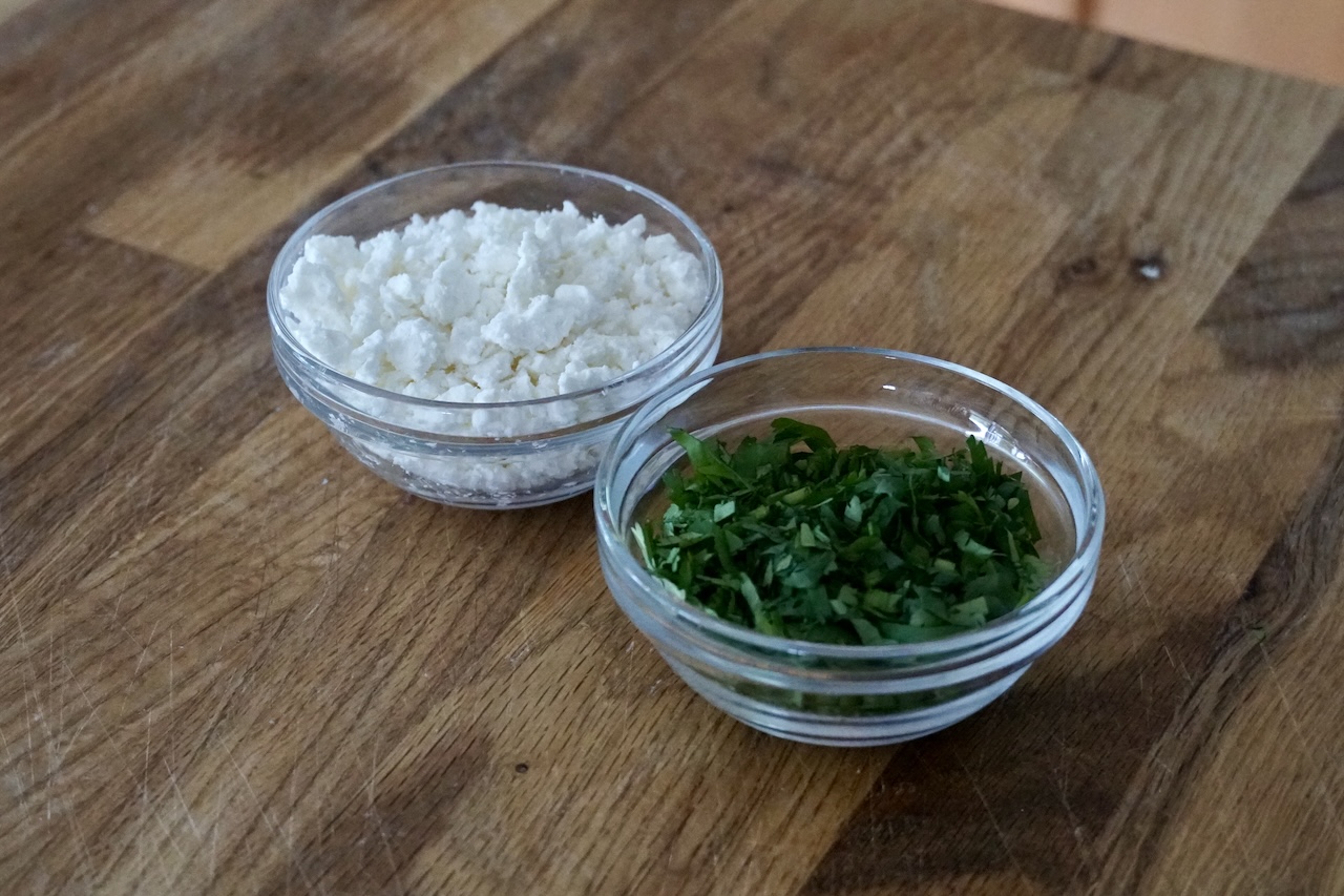 Bowls containing crumbled feta cheese and freshly chopped herbs.