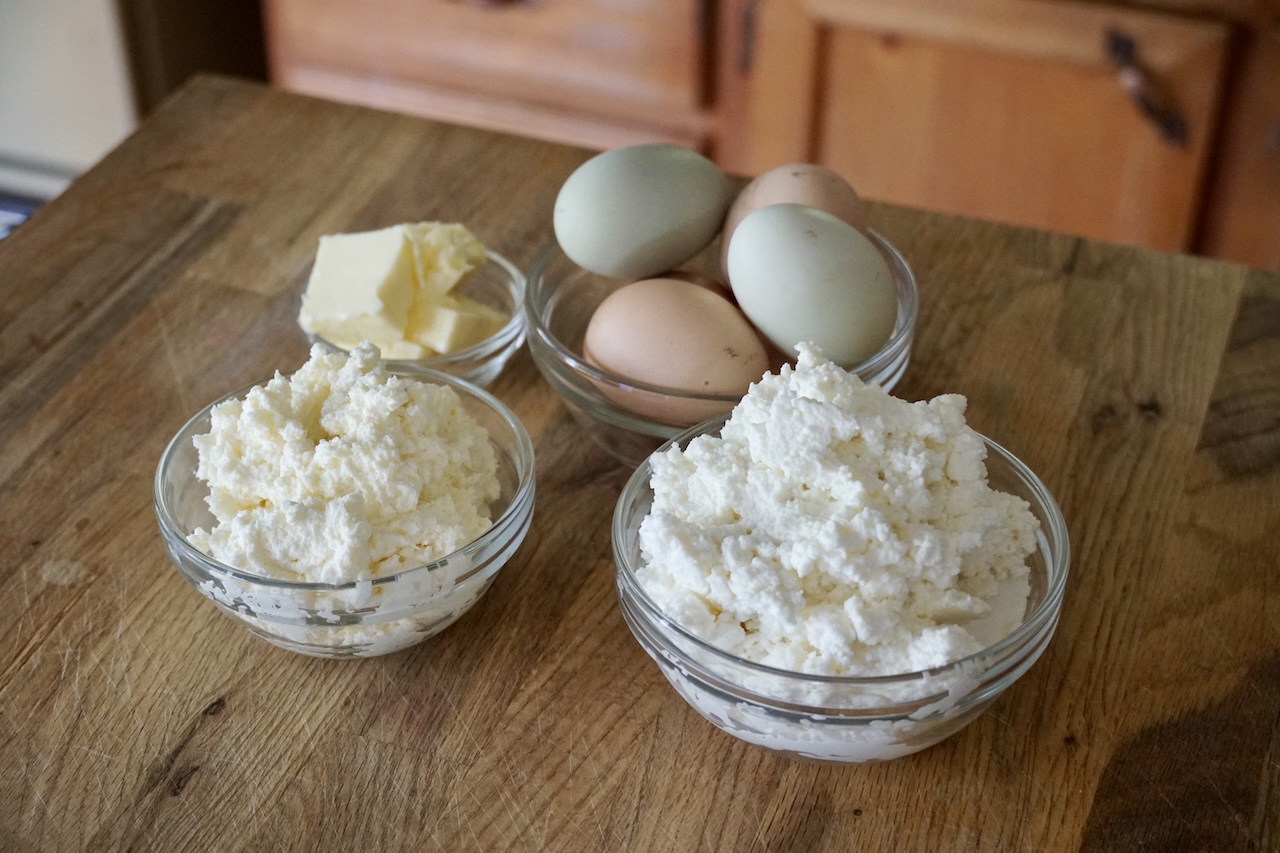 Bowls containing fresh eggs, salted butter, ricotta cheese and creamy kajmak.