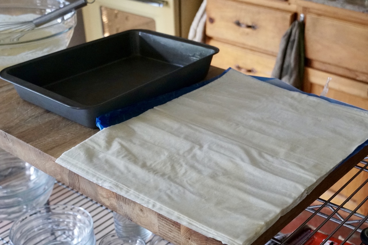 A package of phyllo dough unrolled next to a greased baking pan.