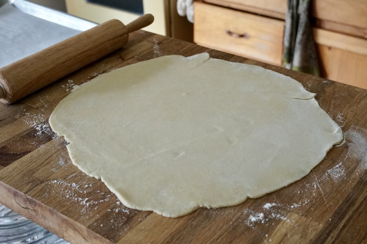 The galette dough rolled out into a large round on a pastry board.