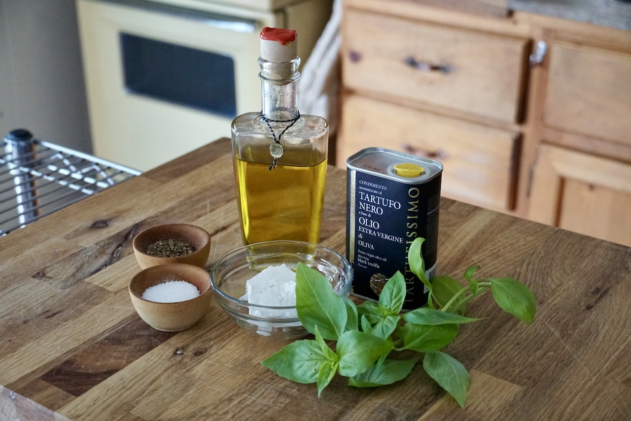 A bottle of olive oil, a tin of truffle oil, feta cheese, salt, pepper and fresh basil leaves for the top of the galette.