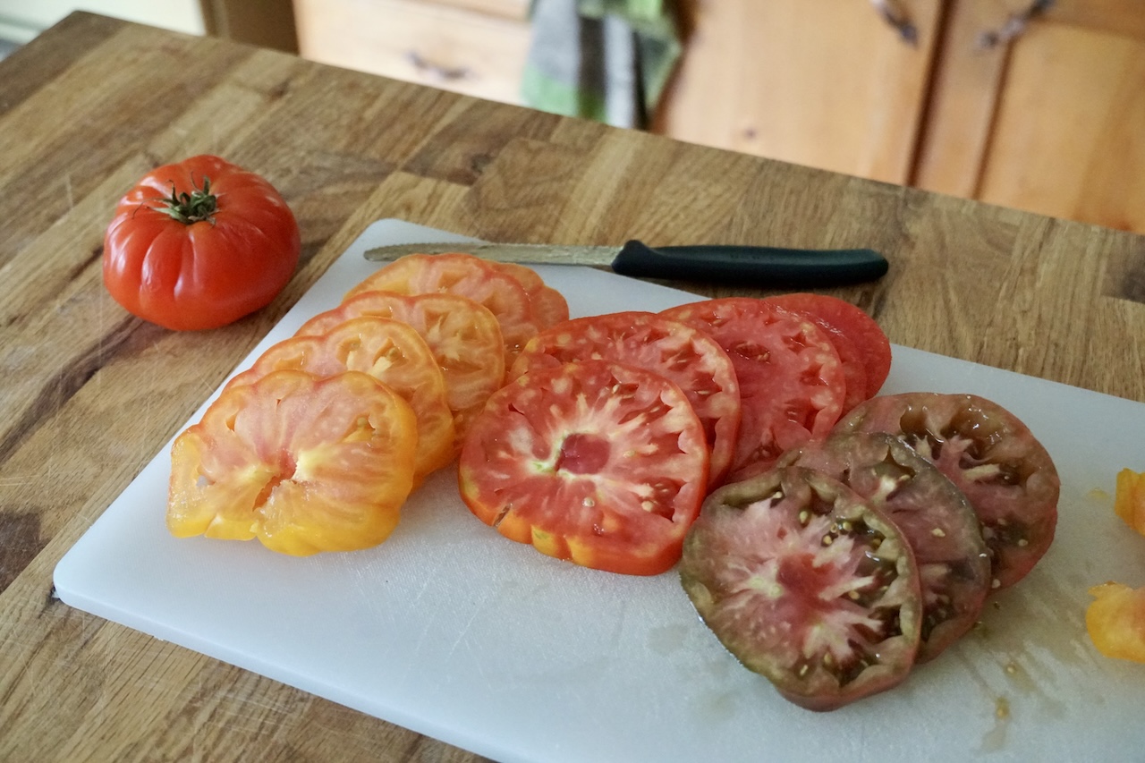 Juicy heirloom tomatoes, thinly sliced, laid out on a cutting board.