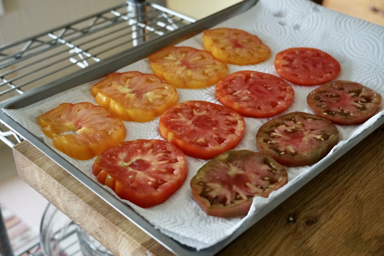 The tomato slices resting on a paper towel-lined baking tray to extract excess juices.
