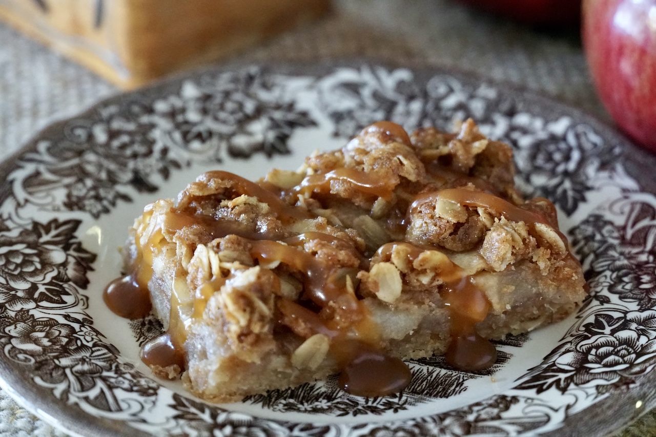 An Apple Pie Crumble Bar drizzled with salted caramel sauce served on a small dessert plate.