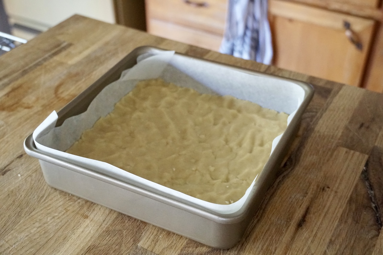 The shortbread base pressed down into a square metal pan lined with parchment paper.