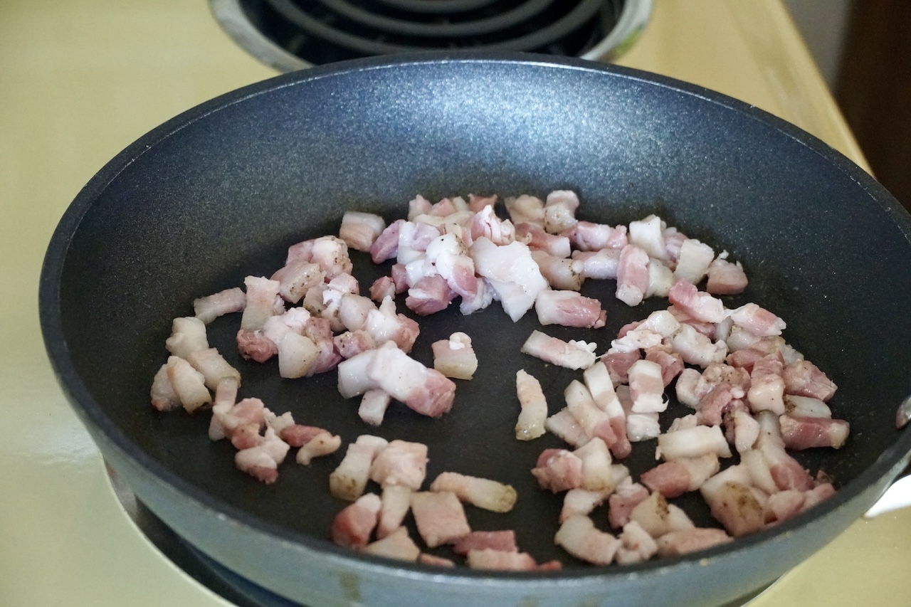 Morsels of pancetta sautéed in a large skillet.