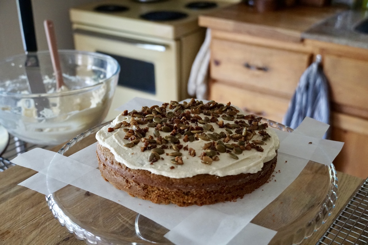 The cake being iced, the first layer topped with a sprinkle of nutty topping.