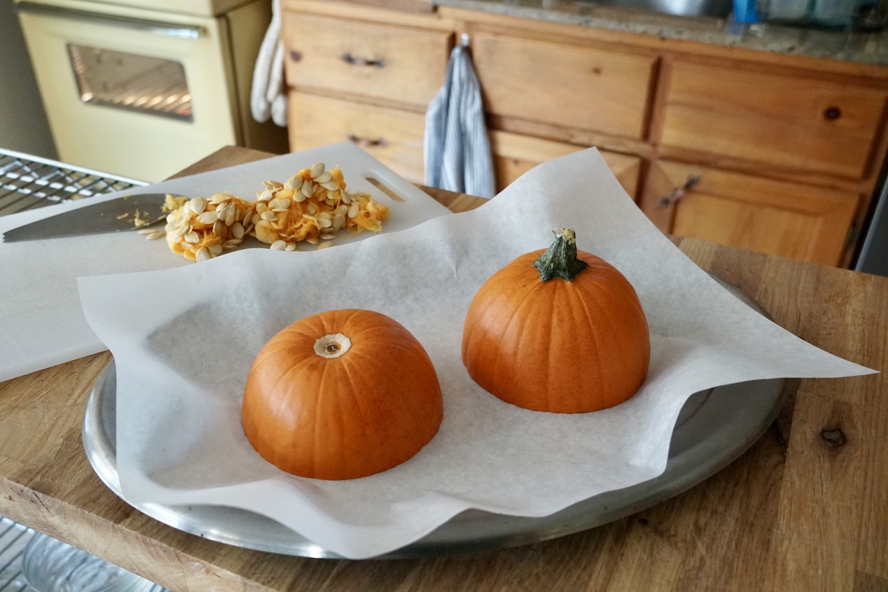 A sugar pumpkin cut in half, resting on a baking tray.