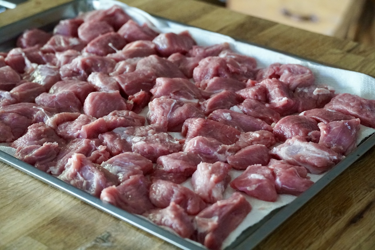 All of the chunks or morsels of meat laid out on a paper-towel lined tray, seasoned with kosher salt and black pepper.