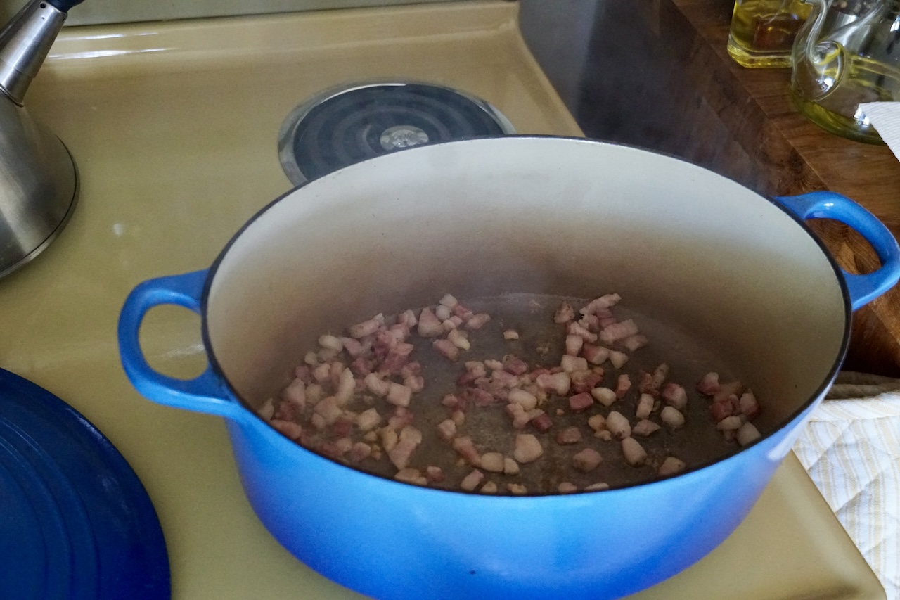 The Dutch oven on stovetop with the pancetta searing within.