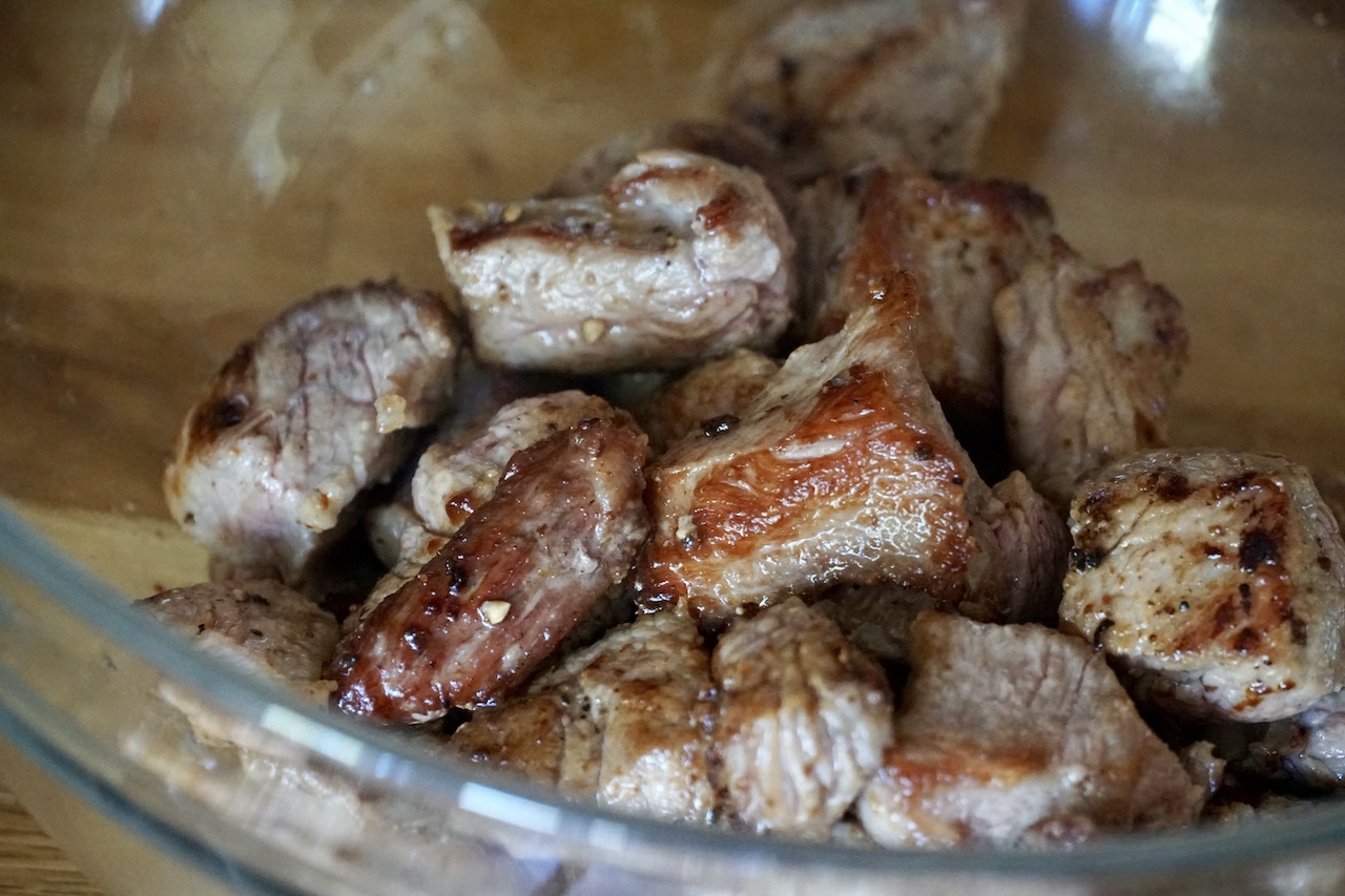 Chunks of veal resting in a glass bowl after being seared.