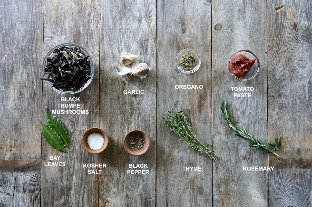 The aromatics laid out on the counter include: fresh herbs, mushrooms, tomato paste, garlic and seasonings.