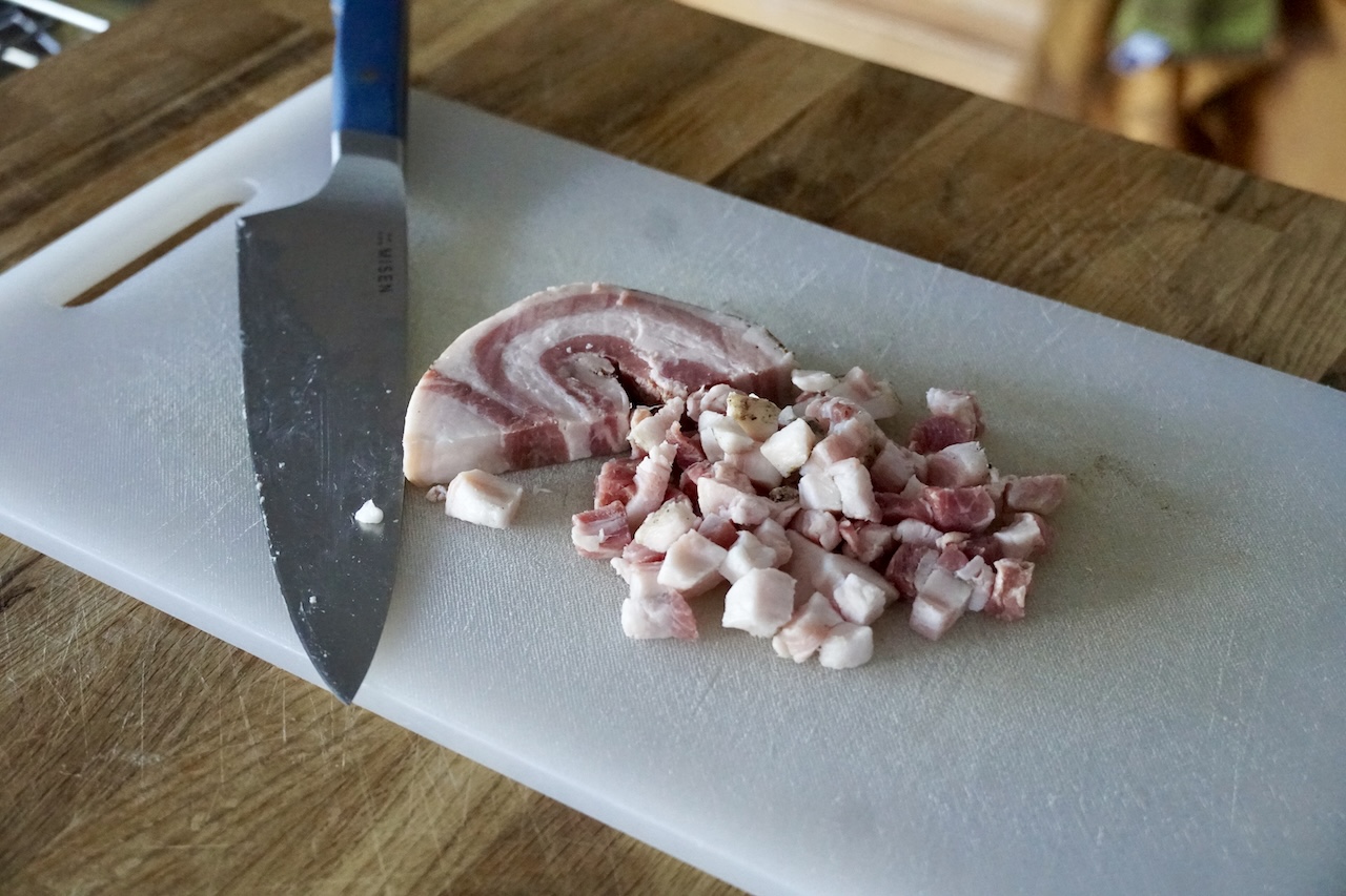 A big chunk of pancetta diced up on a cutting board.